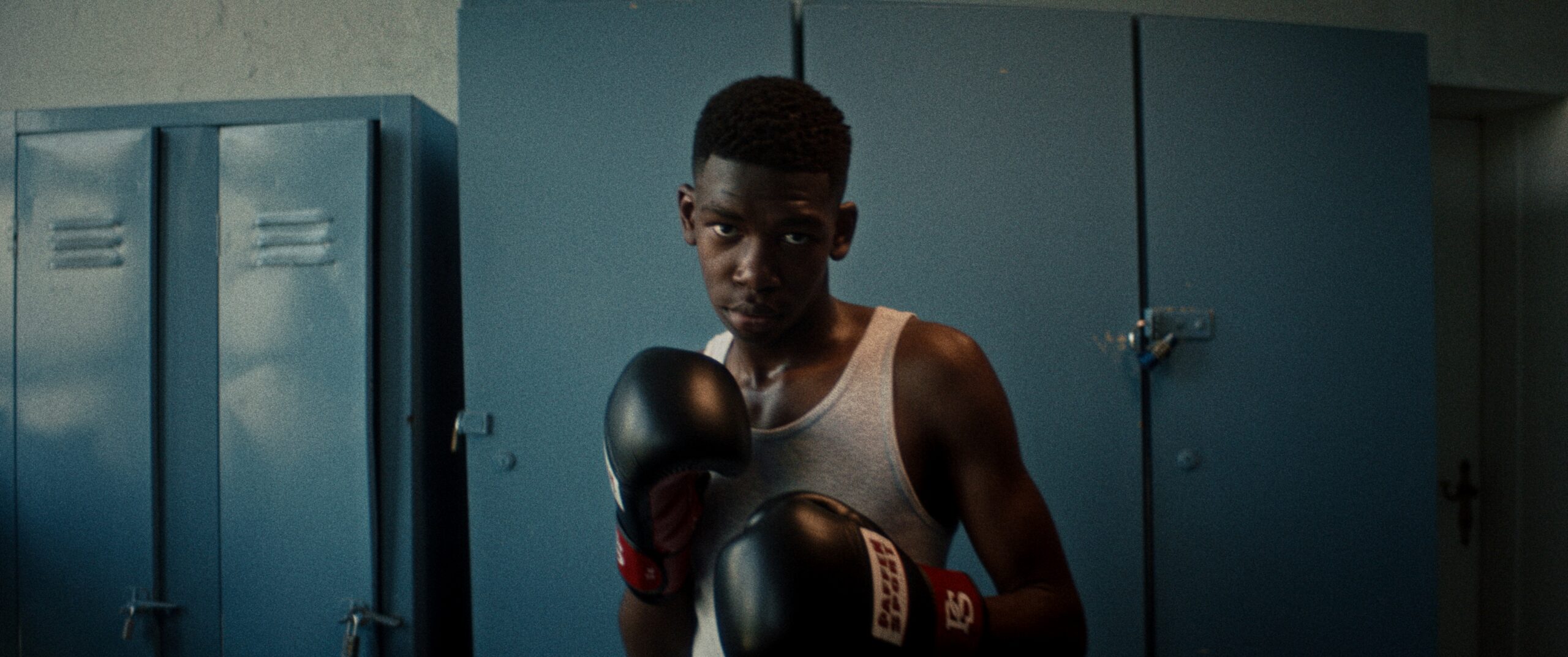 Floyd-Mayweather-URUS-lockers-by-Robert-Wunsch Young boxer with gloves in front of blue lockers.