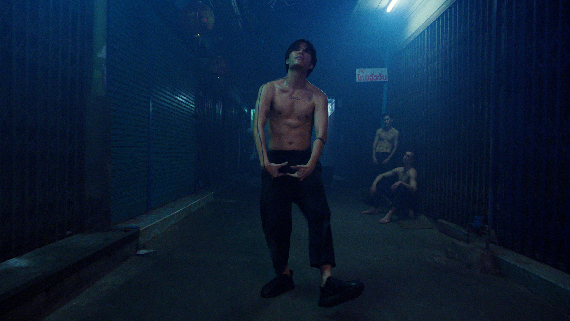 Rita-Ora-x-Tiago-PZK-x-Robin-Schulz-Ill-Be-There-blue-by-Robert-Wunsch Guy dancing shirtless next to closed shops in blue light.