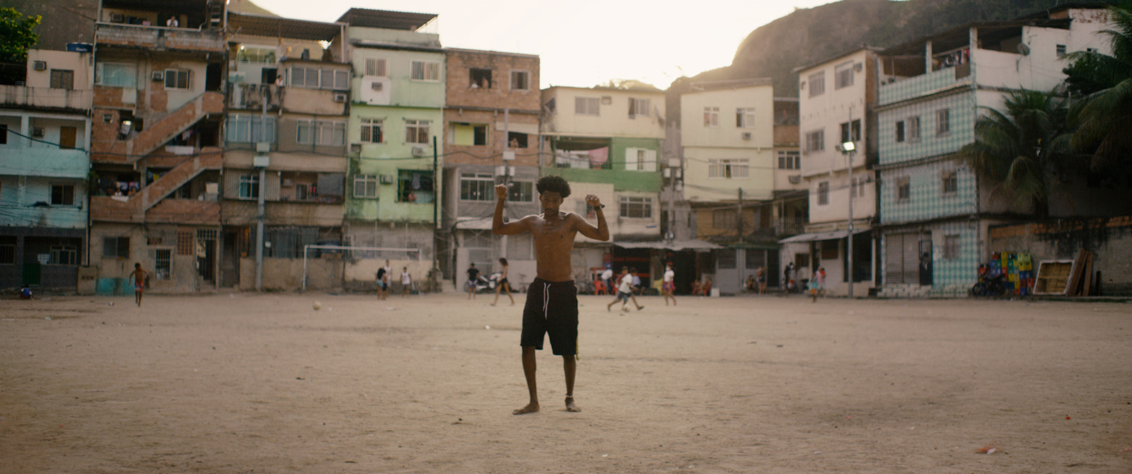 Robin-Schulz-Ft-Wes-Alane-dance-neighbourhood-by-Robert-Wunsch Guy dancing on sand barefoot and shirtless in a poorly neighbourhood with kids playing football